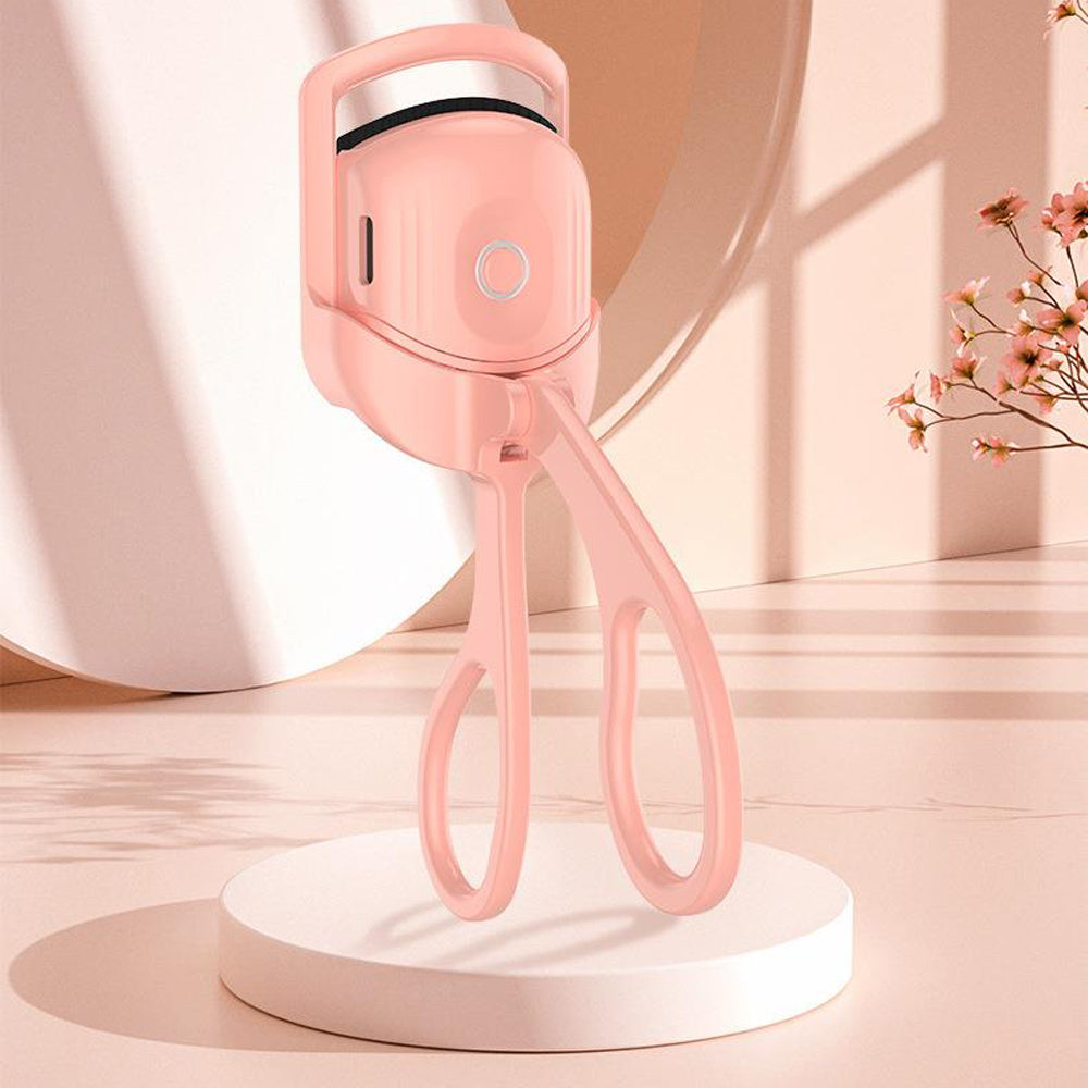 A pink portable electric heated eyelash curler placed on a white stand, designed for beauty and personal care.